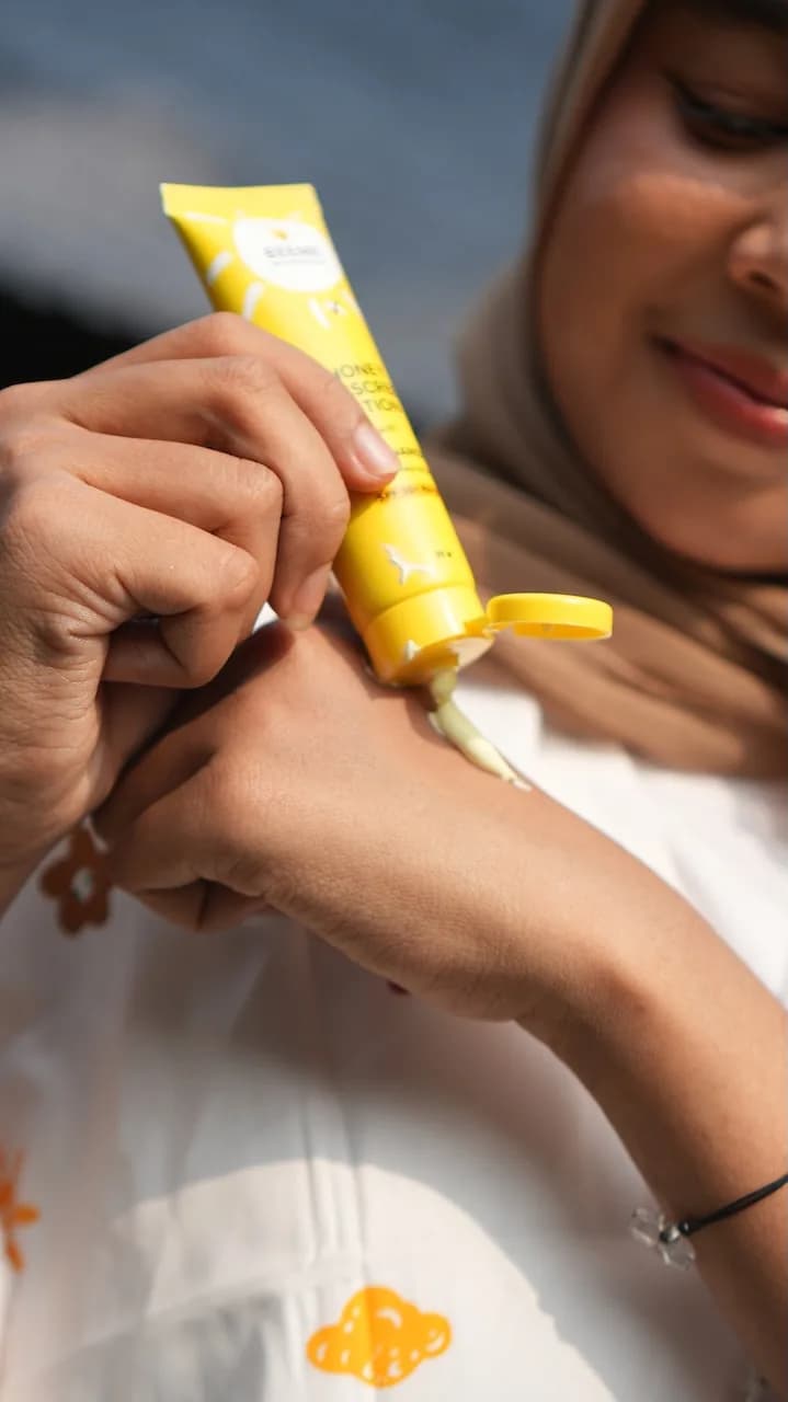 A creator squeezing a yellow sunscreen tube onto the back of her hand