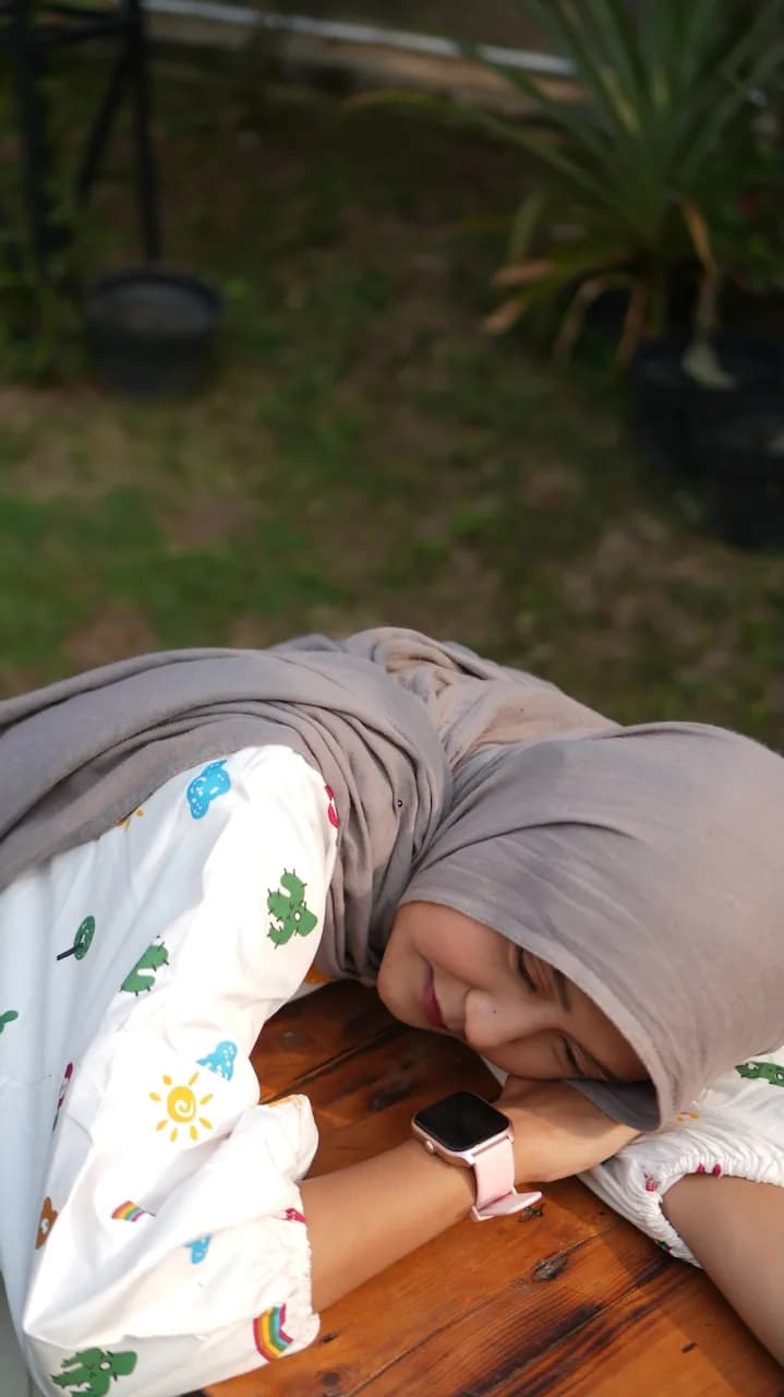A creator resting her head on a wooden table, wearing a pink smartwatch