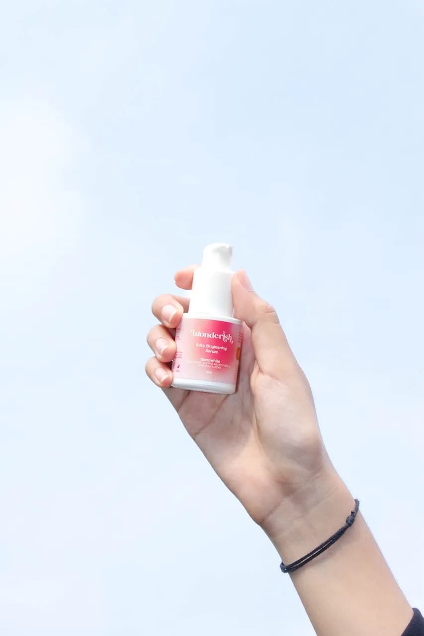 A hand holding a Wonderish brightening serum against a pale blue sky