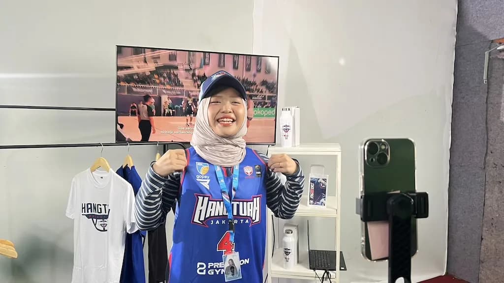 A host in a Hangtuah Jakarta jersey livestreaming merchandise to a phone rig