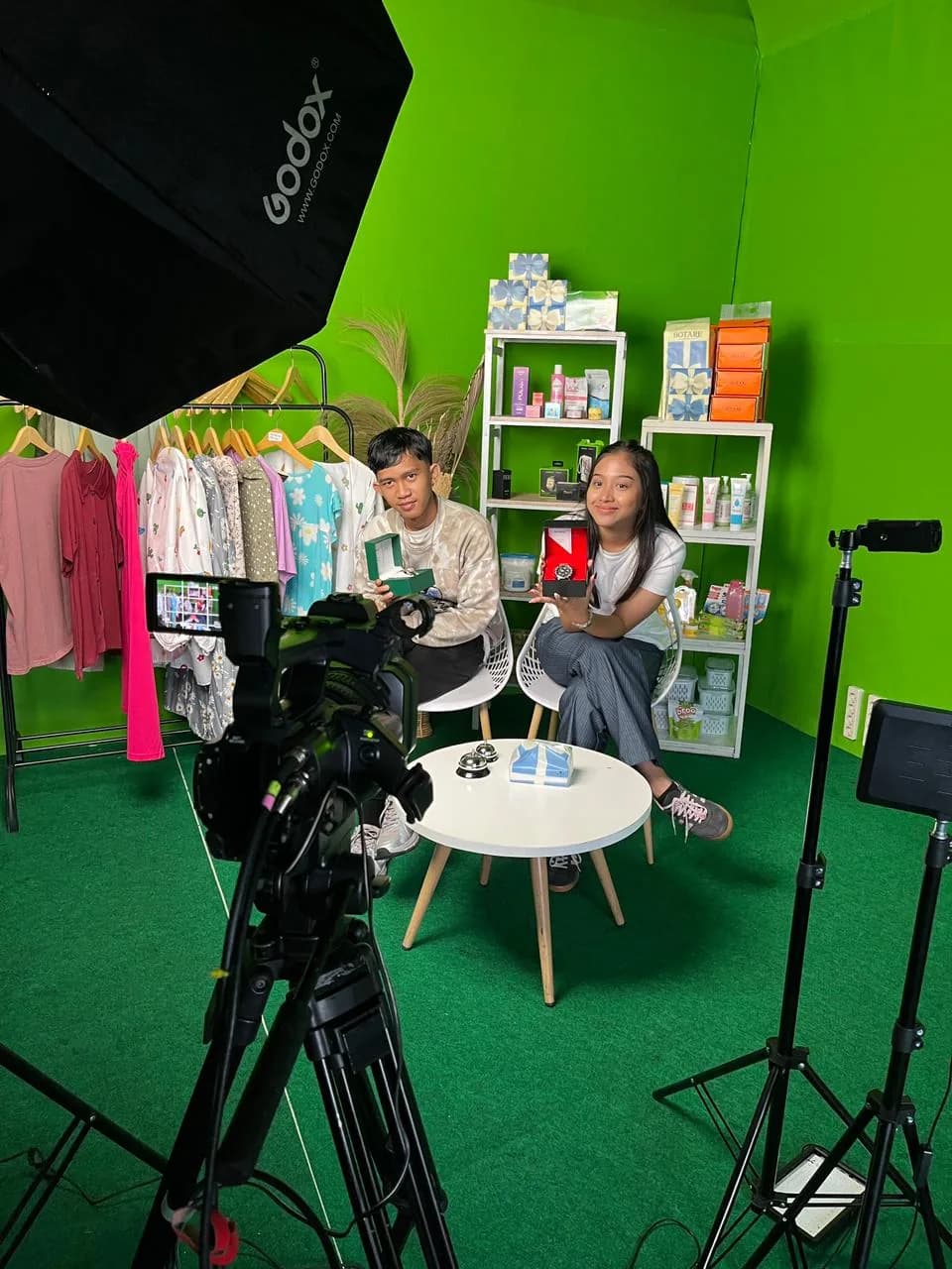 Hosts showing watches on a green-screen set, framed by a studio camera and softbox