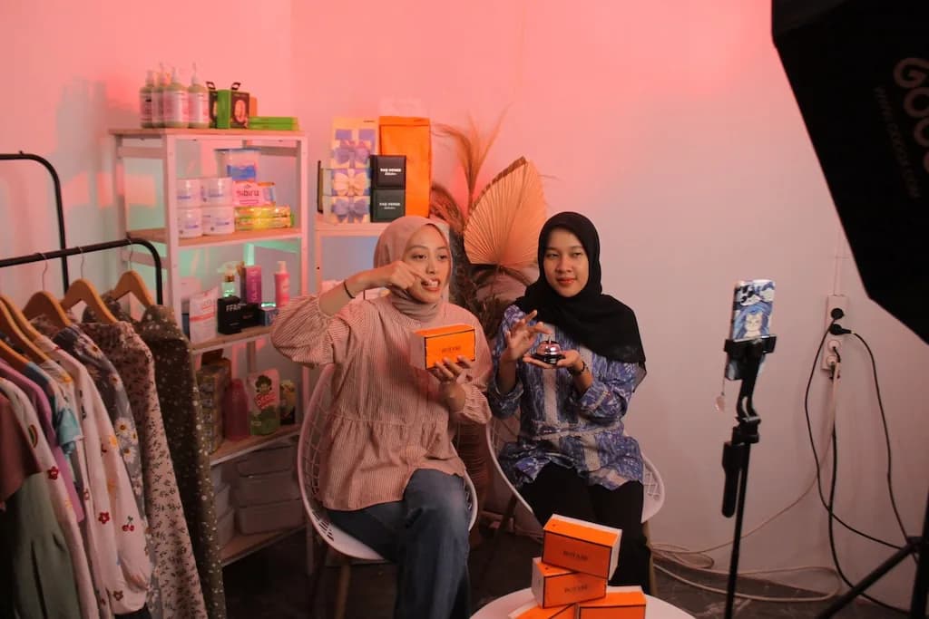 Two hosts demonstrating skincare products under pink studio light