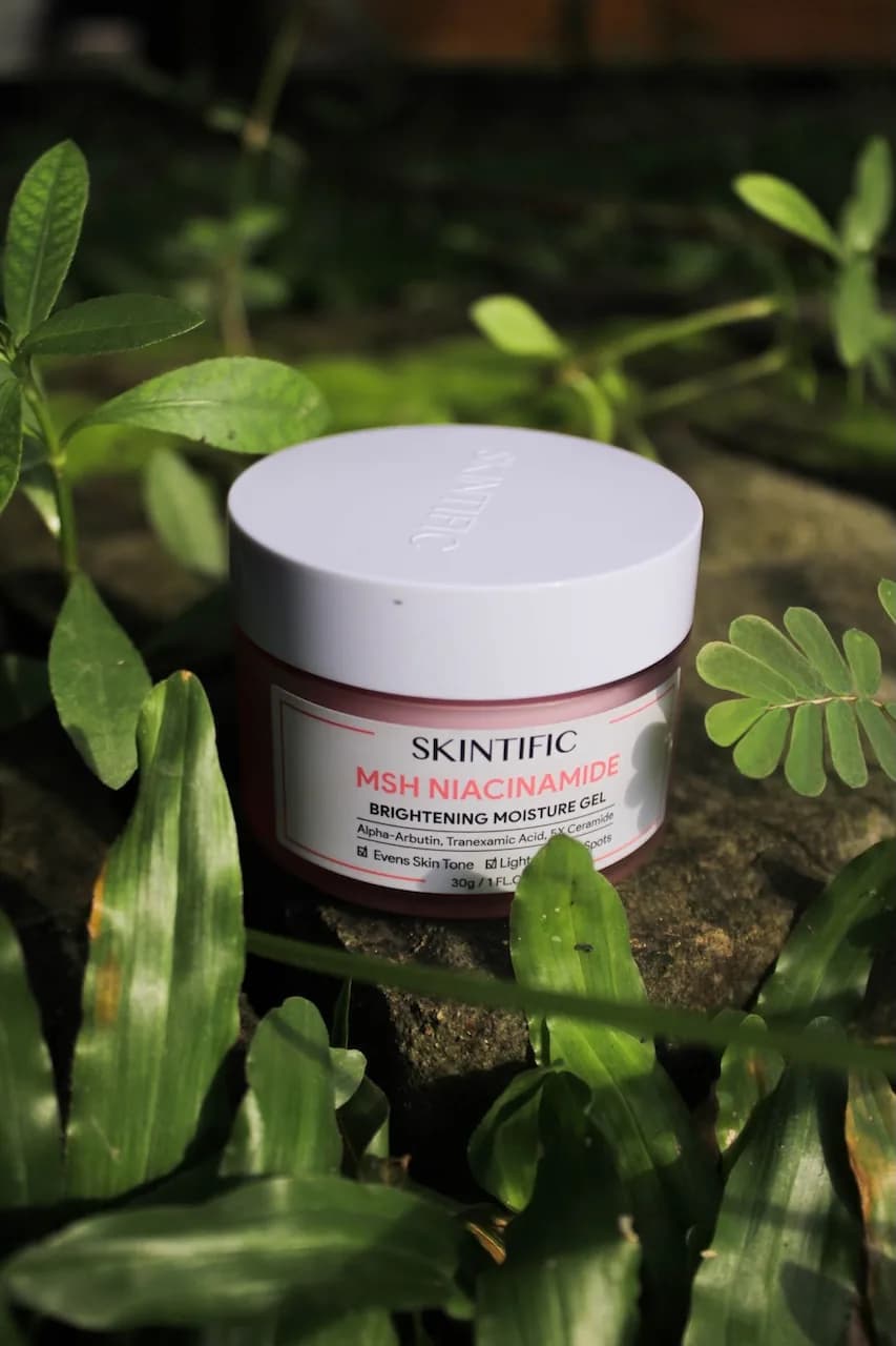 A jar of Skintific brightening moisture gel set among green leaves