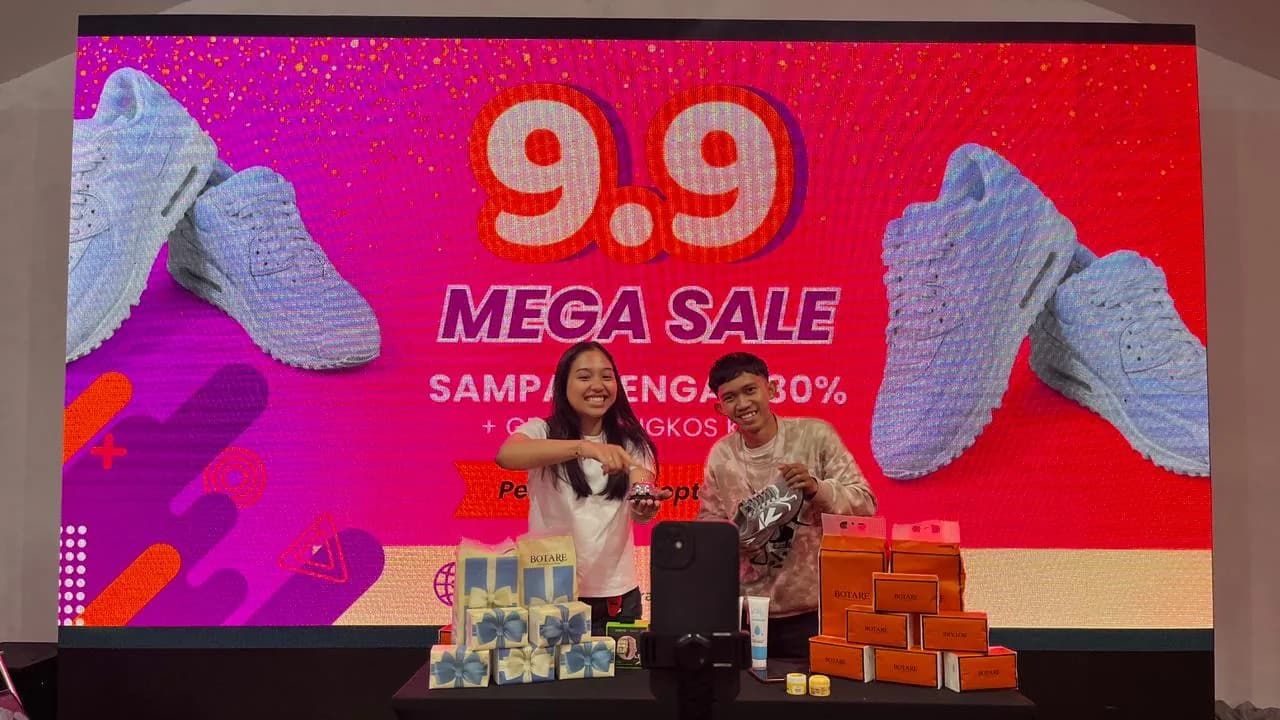 Two hosts presenting products live in front of a 9.9 Mega Sale LED wall